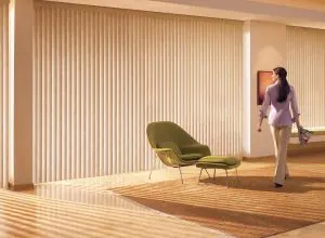 Beige vertical blinds across a wall of windows with a green lounge chair