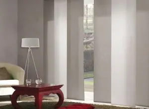 Light grey sliding panels at a glass door beside a red side table