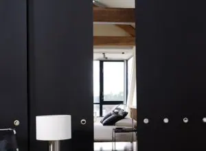 Black sliding panels partly open onto a living space with a white lamp