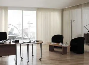 Cream vertical blinds in a bright office with black armchairs and desks