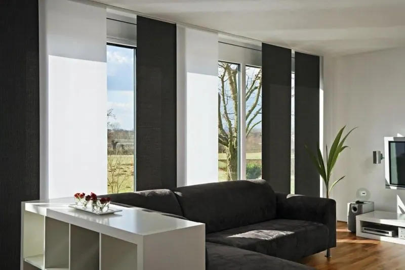 Dark grey and white sliding panels at large windows beside a dark sofa