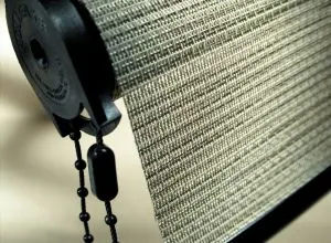 Close-up of a woven grey roller shade with black bead chain and mechanism