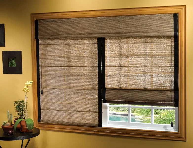 Natural woven Roman shades on a wood-framed window with yellow walls