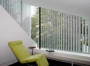 White vertical blinds on a slanted window with a lime green chair
