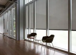 Grey solar roller shades on floor-to-ceiling windows with two chairs