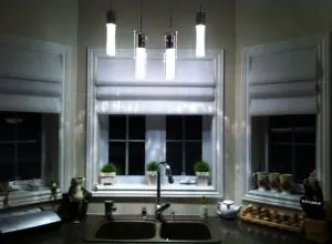 Pale grey Roman shades on a kitchen window above a double sink