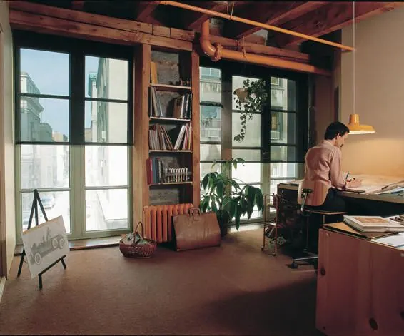 Loft-style home office with tall windows and a person at a desk
