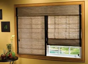 Brown woven Roman shades, one raised, in a window with yellow wall