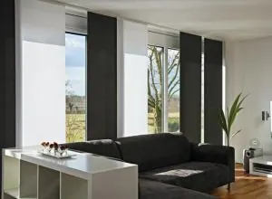 Black and white sliding panels at tall windows over a charcoal sofa