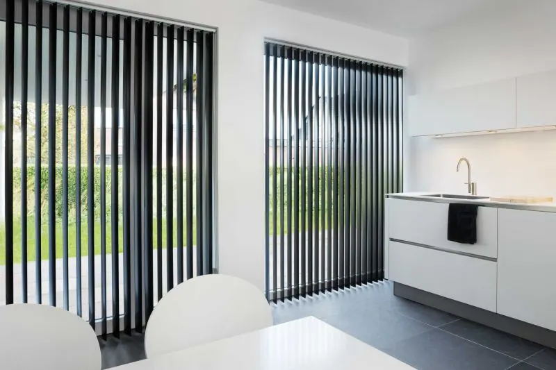 Black vertical blinds on glass doors in a modern white kitchen