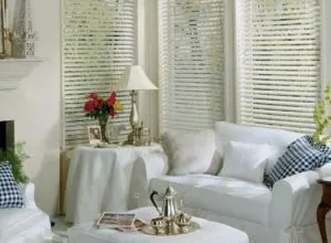 White horizontal blinds on corner windows above white slipcovered sofas