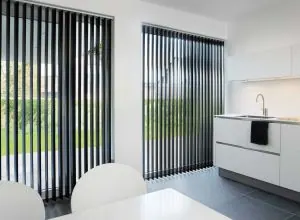 Open black vertical blinds facing the garden beside a white kitchen counter
