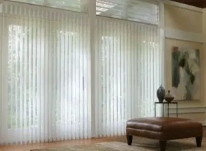 Sheer white vertical blinds on tall windows beside a leather ottoman