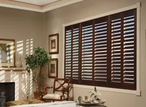 Dark brown wood shutters on a large window in a room with a fireplace