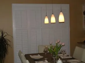 White shutters covering a wall in a dining room with pendant lights