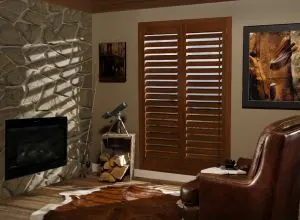 Reddish wood shutters next to a textured stone wall and electric fireplace