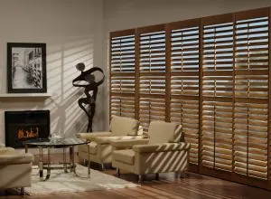Wood shutters across a large window with cream armchairs and fireplace