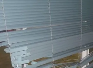 Damaged blue-grey horizontal blind with broken slats and loose cords