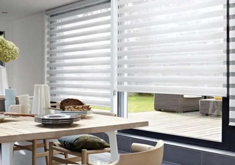 White zebra shade half lowered on a patio door above a set table