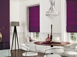 Plum purple Roman shades in a white dining room with a glass chandelier