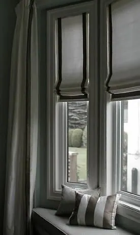 Dark grey Roman shades with black trim and a grey curtain at a window