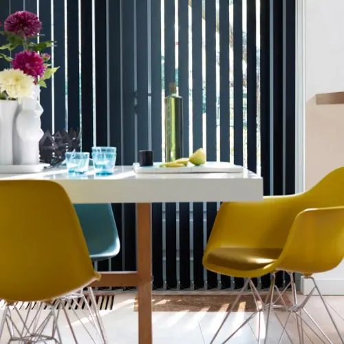 Navy vertical blinds behind a white table and mustard yellow chairs