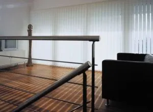 White vertical blinds near a railed landing and black armchair