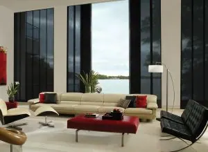 Black sliding panels on tall windows in a cream living room by a lake