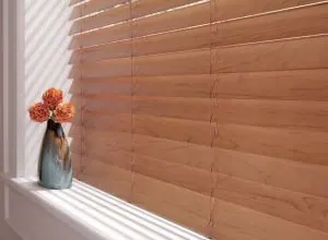 Close-up of honey wood horizontal blind with orange flowers on the sill