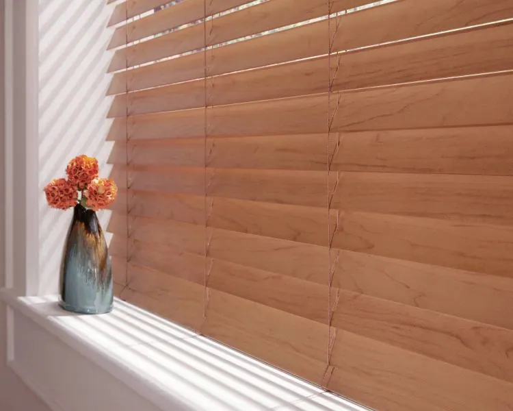 Close view of light wood horizontal blind slats above a flowered sill