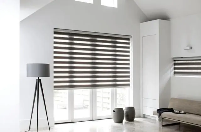 Dark grey zebra shade on a glass door in a white room with a tripod lamp