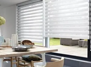 White zebra shades on a glass door above a dining table by a deck