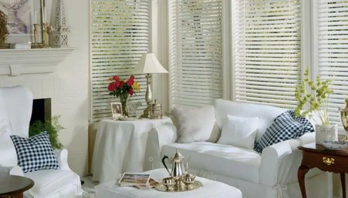 White horizontal blinds on corner windows above white armchairs