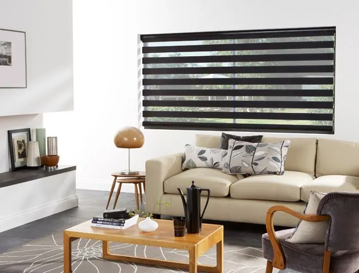 Black zebra shade on a white wall above a cream sofa and wood table