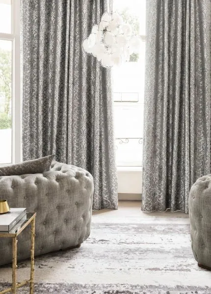Grey damask-pattern curtains beside a tufted armchair and bright window