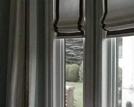 Grey Roman shades with black borders and a grey curtain at tall windows