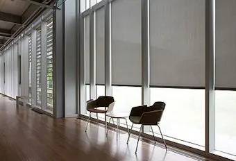 Large grey roller shades on floor-to-ceiling glass with two low chairs