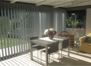 Grey vertical blinds in a sunroom with a dining table and chairs