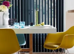 Navy vertical blinds behind yellow chairs and a white dining table