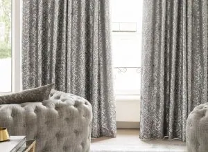 Grey damask curtains on both sides of a window with a tufted chair