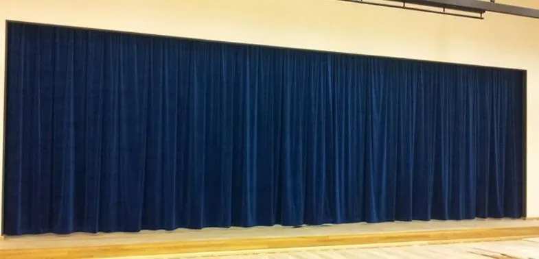 Long navy pleated drapery across a stage with a wood floor