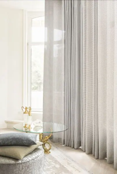 White sheer floor-length curtain beside a glass table and cushions